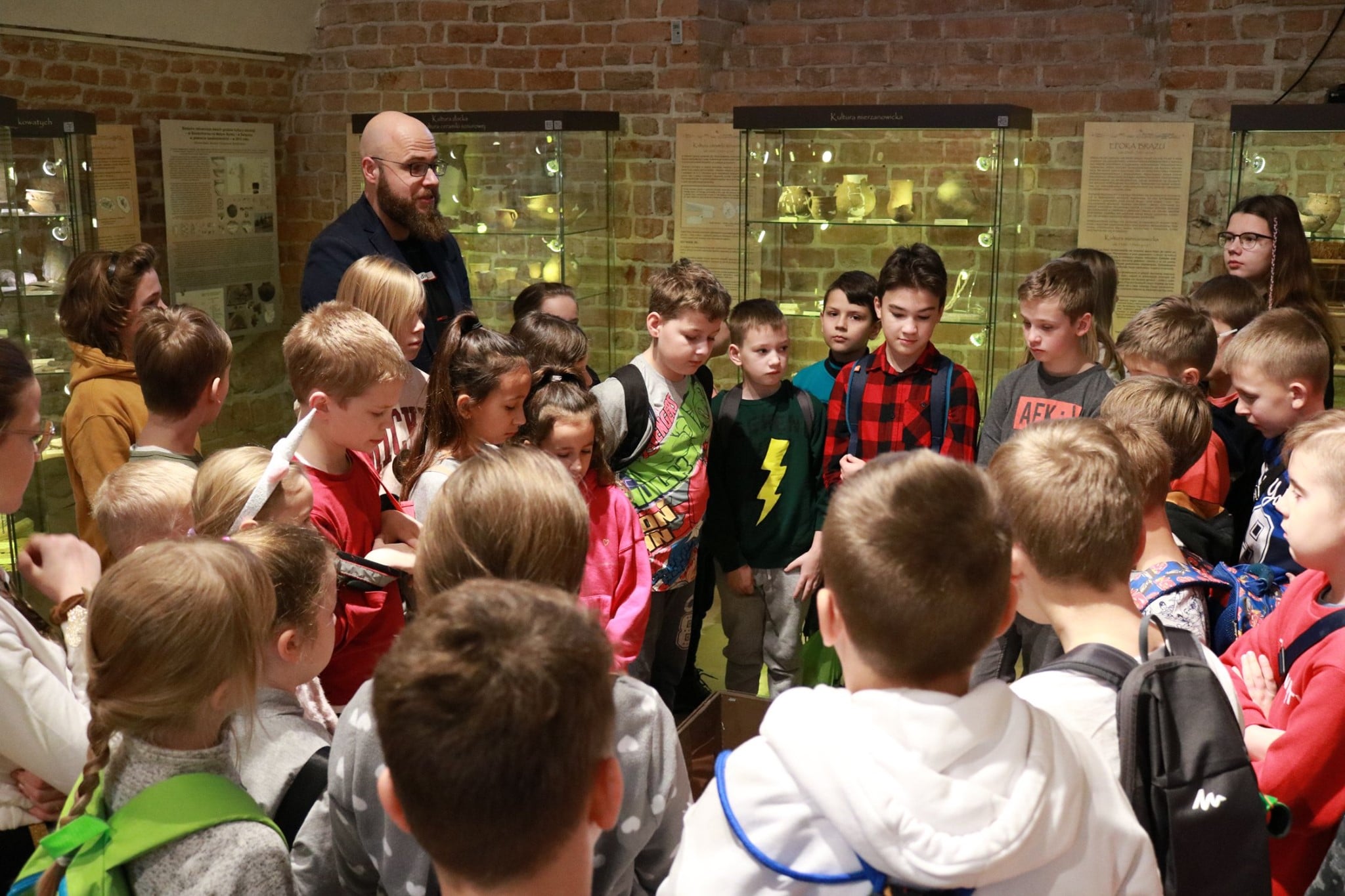 Dyrektor muzeum okręgowego w sandomierzu wraz ze słuchaczami muzealnego uniwersytetu dziecieciego na tle wystawy w sandomierskim muzeum